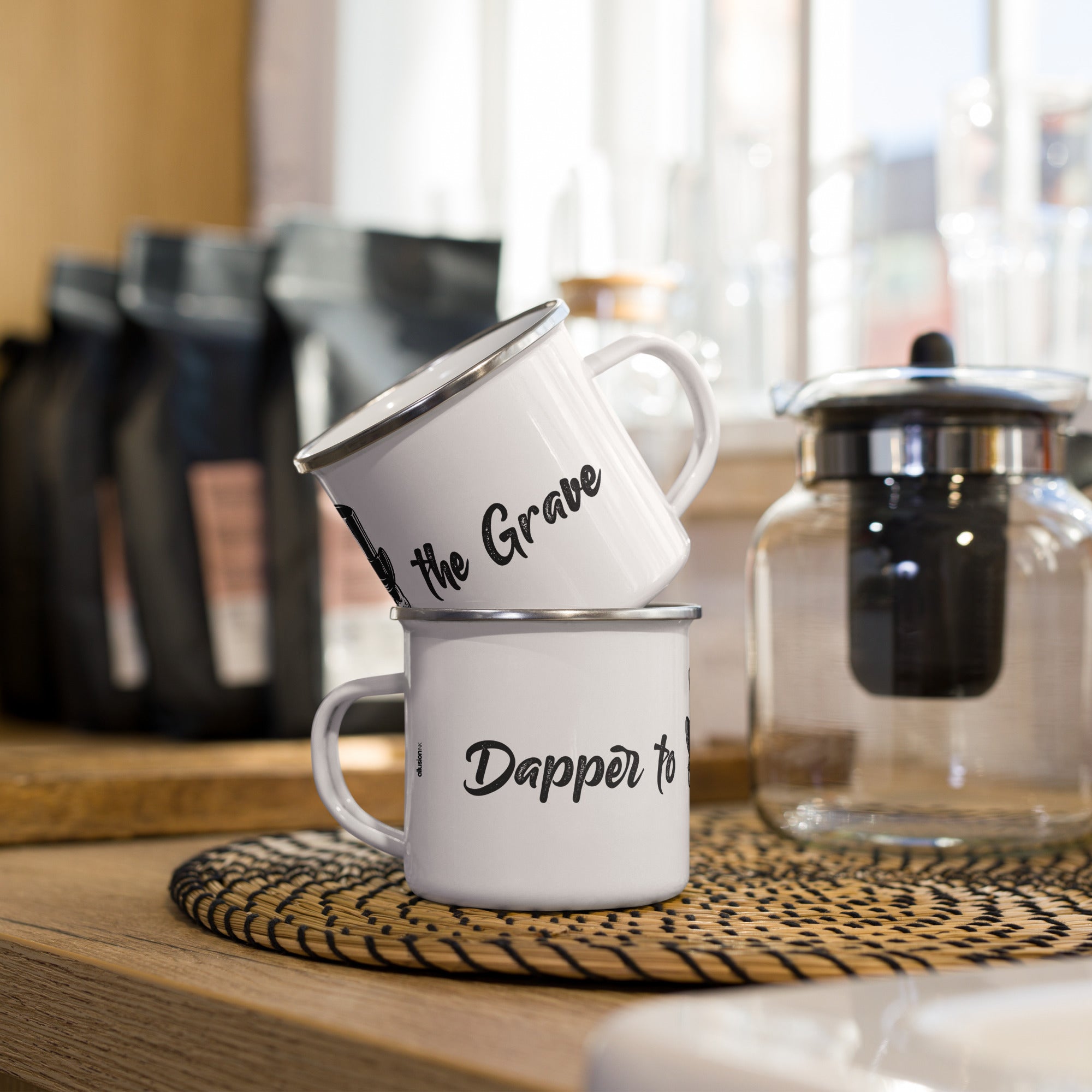 Two stacked "Dapper to the Grave" enamel mugs placed on a modern kitchen counter.