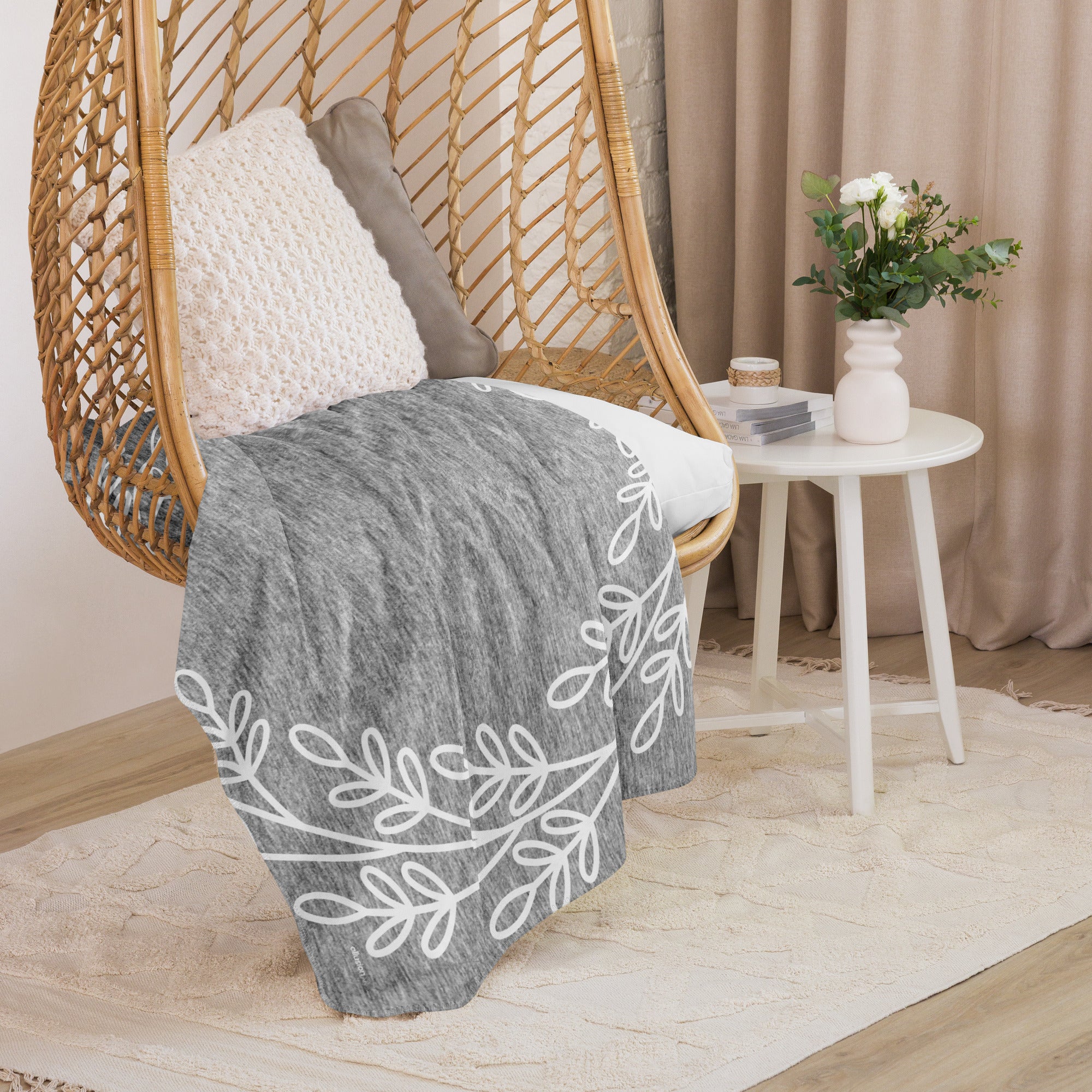 Gray sherpa blanket with a white wreath pattern draped over a hanging chair in a cozy room setting.