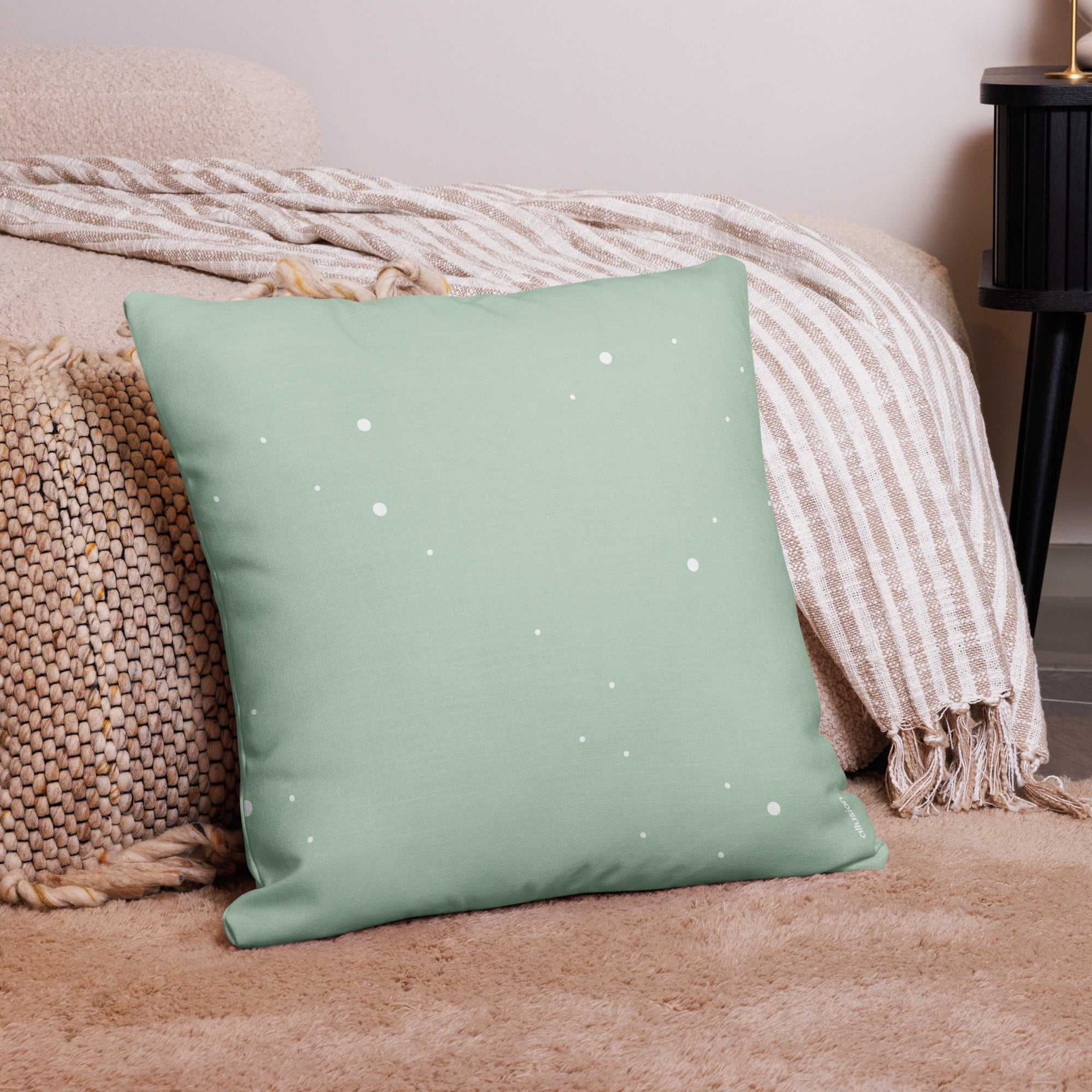 Minimalist mint green decorative pillow with white snowflake accents, styled on a neutral beige rug and striped throw.