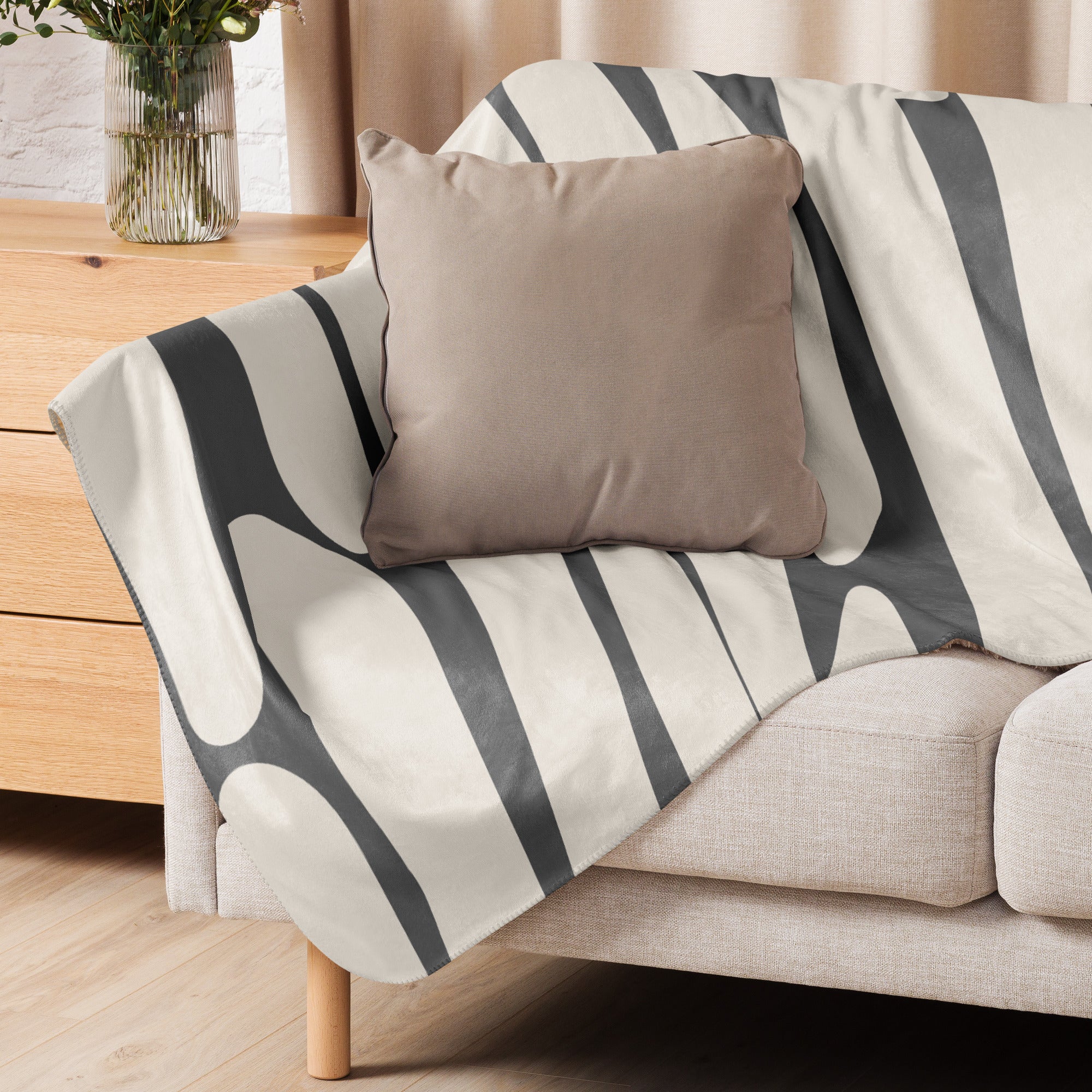 A neutral-toned sherpa blanket with an abstract charcoal and ivory pattern draped over a beige sofa, styled with a tan pillow.