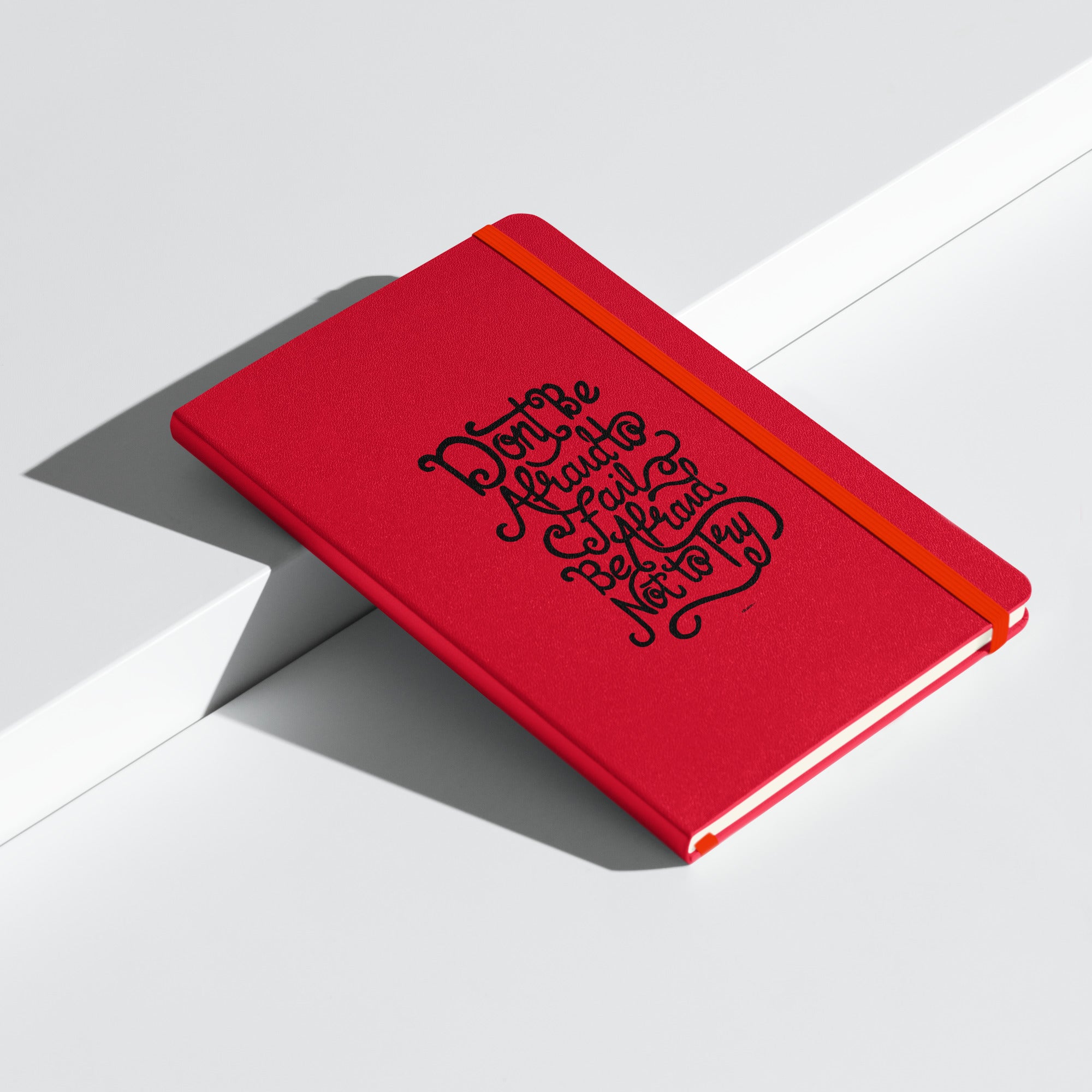 Red hardcover notebook with the inspirational quote 'Don't be afraid to fail, be afraid not to try' on the front laying down.