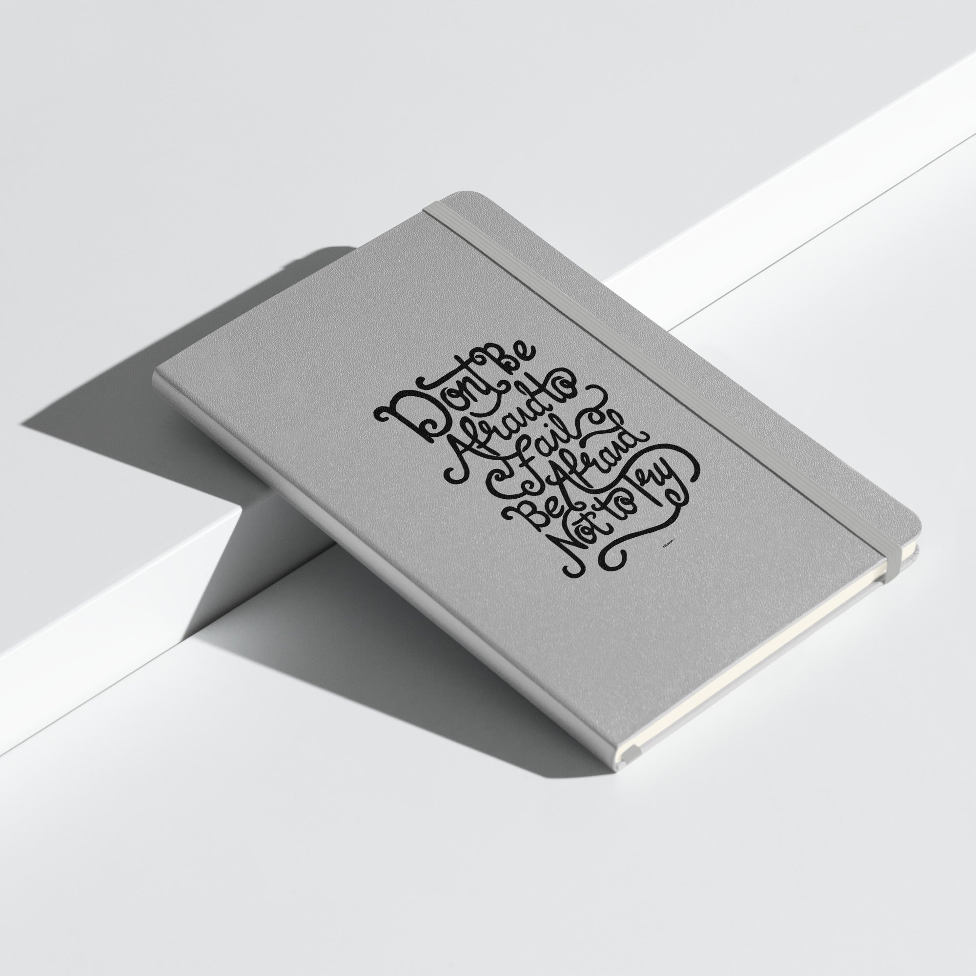 Silver notebook with elegant design and motivational quote 'Don't be afraid to fail, be afraid not to try' on the front.