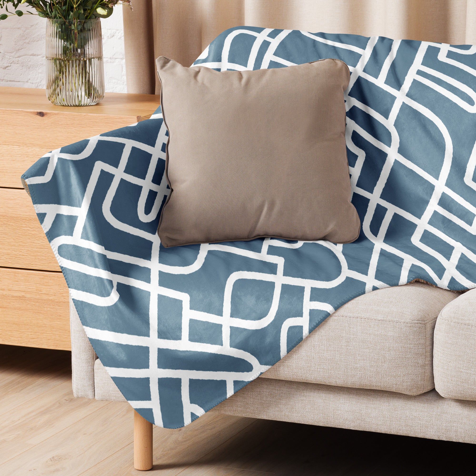 A sherpa blanket with a teal and white geometric design draped over a sofa, styled with a tan pillow.