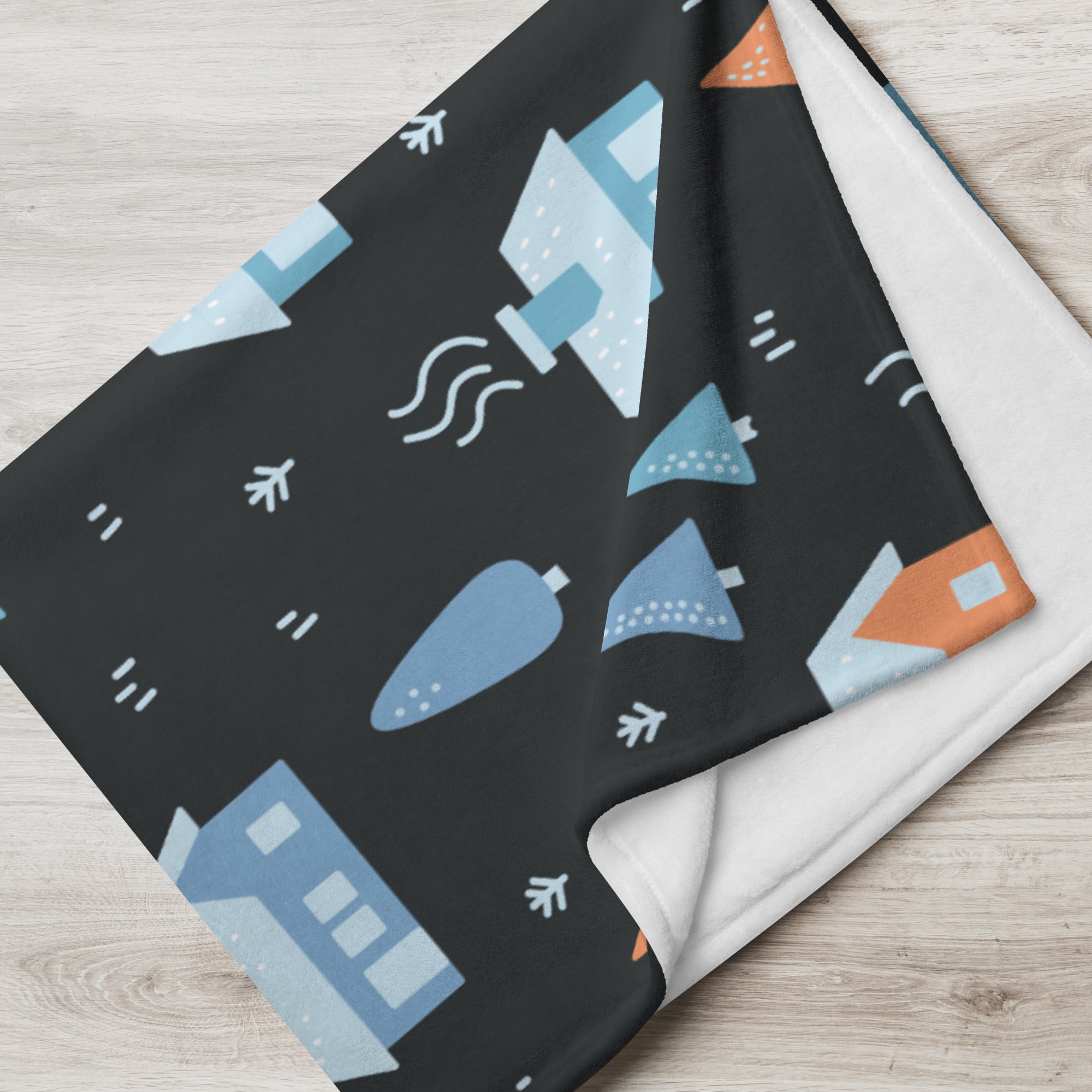 Detailed view of the throw blanket with a winter village pattern, showcasing vibrant orange and blue house illustrations on a dark background.